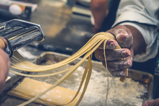 Chef de cozinha industrial preparando massa de macarrão com cilindro para massas e forma untada com farinha, simbolizando a dúvida de como montar uma cozinha industrial